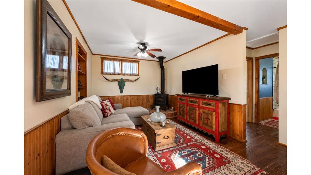 117 Reading Avenue North Center Point, TX 78010 - Photo 12 of 20 Cozy living area featuring a freestanding wood-burning stove with a brick base, wood-finish flooring, exposed ceiling beams, and a ceiling fan