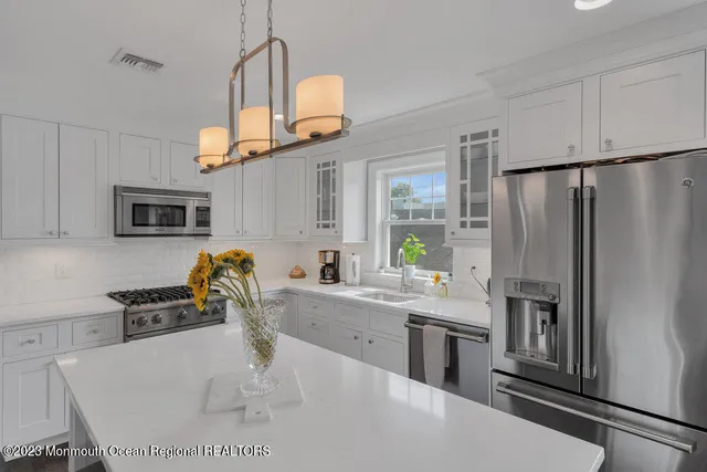 a kitchen with stainless steel appliances granite countertop a sink a stove a refrigerator a microwave oven with white cabinets and wooden floor