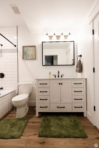 924 Country Lane Farmington, UT 84025 - Photo 61 of 91 Bathroom featuring a white subway tile shower surround with a decorative accent band, a built-in bathtub, a white vanity with multiple drawers and cabinet storage, a white countertop, and wood-finish flooring