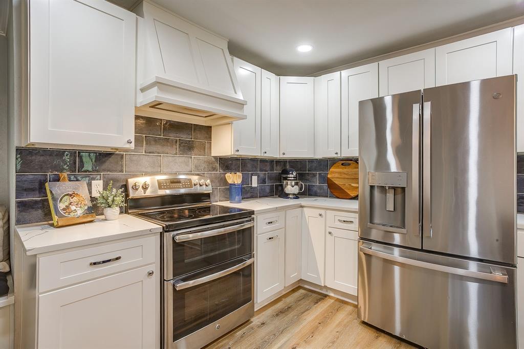 408 Jeri Ridge Road Willow Park, TX 76087 - Photo 12 of 38 White shaker cabinetry with polished nickel hardware, stone countertops, a tiled backsplash, stainless steel appliances, and wood-finish flooring