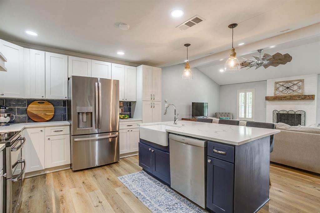 408 Jeri Ridge Road Willow Park, TX 76087 - Photo 13 of 38 Kitchen featuring a large center island with a farmhouse sink, stainless steel appliances, white cabinetry, dark subway tile backsplash, and wood-finish flooring