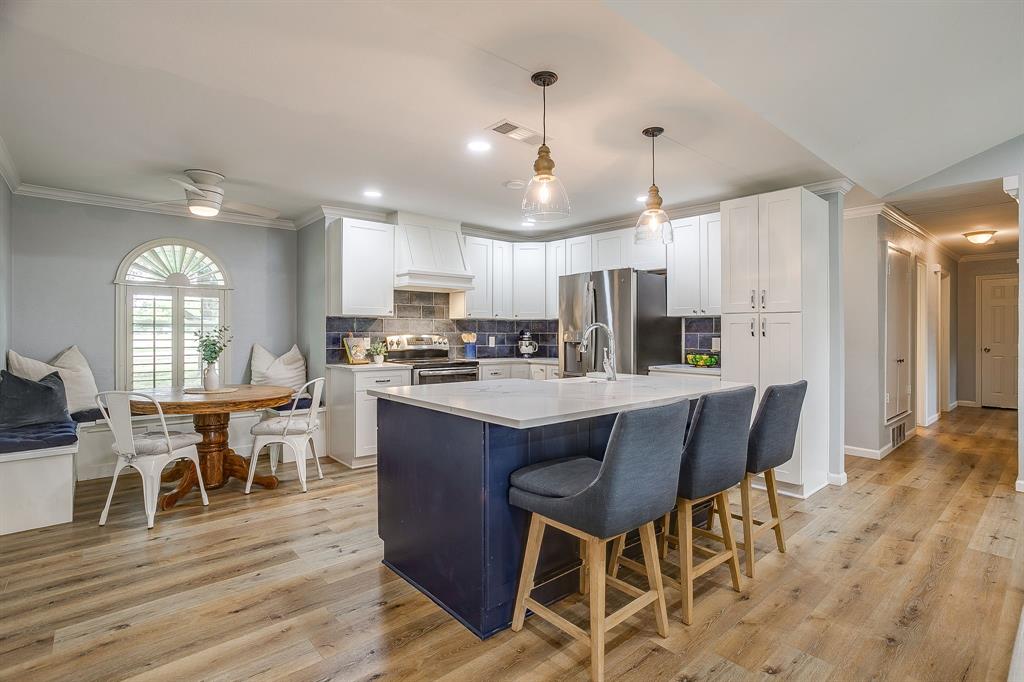 408 Jeri Ridge Road Willow Park, TX 76087 - Photo 9 of 38 Open-concept kitchen featuring an island with counter seating, white cabinetry, integrated stainless steel appliances, wood-finish flooring, and a built-in dining nook with an arched window