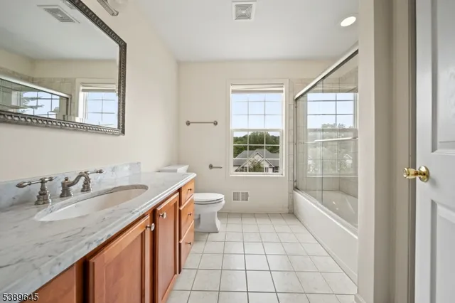 a bathroom with a granite countertop sink a toilet a mirror and next to a window