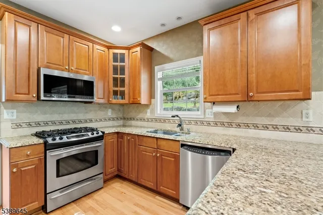 a kitchen with stainless steel appliances granite countertop wooden cabinets a stove top oven a sink and dishwasher with wooden floor
