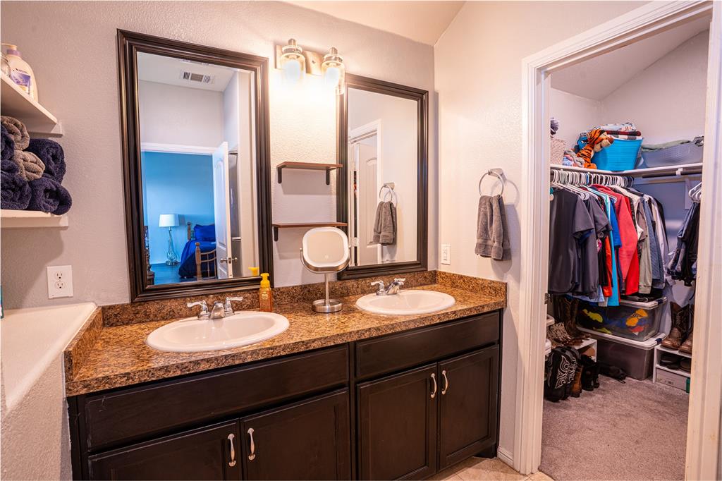753 Rutherford Drive Crowley, TX 76036 - Photo 19 of 26 Bathroom vanity featuring dual sinks, a speckled countertop, and dark wood-finish cabinetry