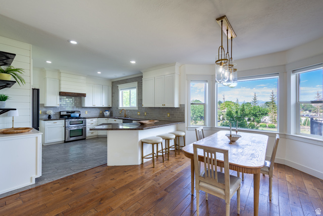 868 Braddock Lane Alpine, UT 84004 - Photo 21 of 64 Bright kitchen and dining area featuring hardwood flooring, white cabinetry, stainless steel appliances, a tile backsplash, and a breakfast bar
