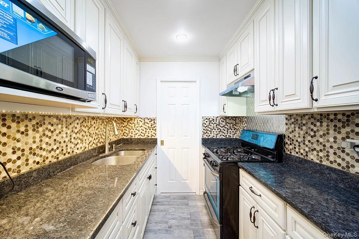 99-05 59th Avenue, Unit 2A Queens, NY 11368 - Photo 5 of 14 a kitchen with granite countertop a stove a sink and a microwave