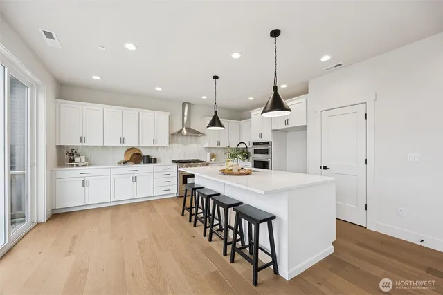 a kitchen with stainless steel appliances kitchen island granite countertop a sink a stove a refrigerator and white cabinets with wooden floor