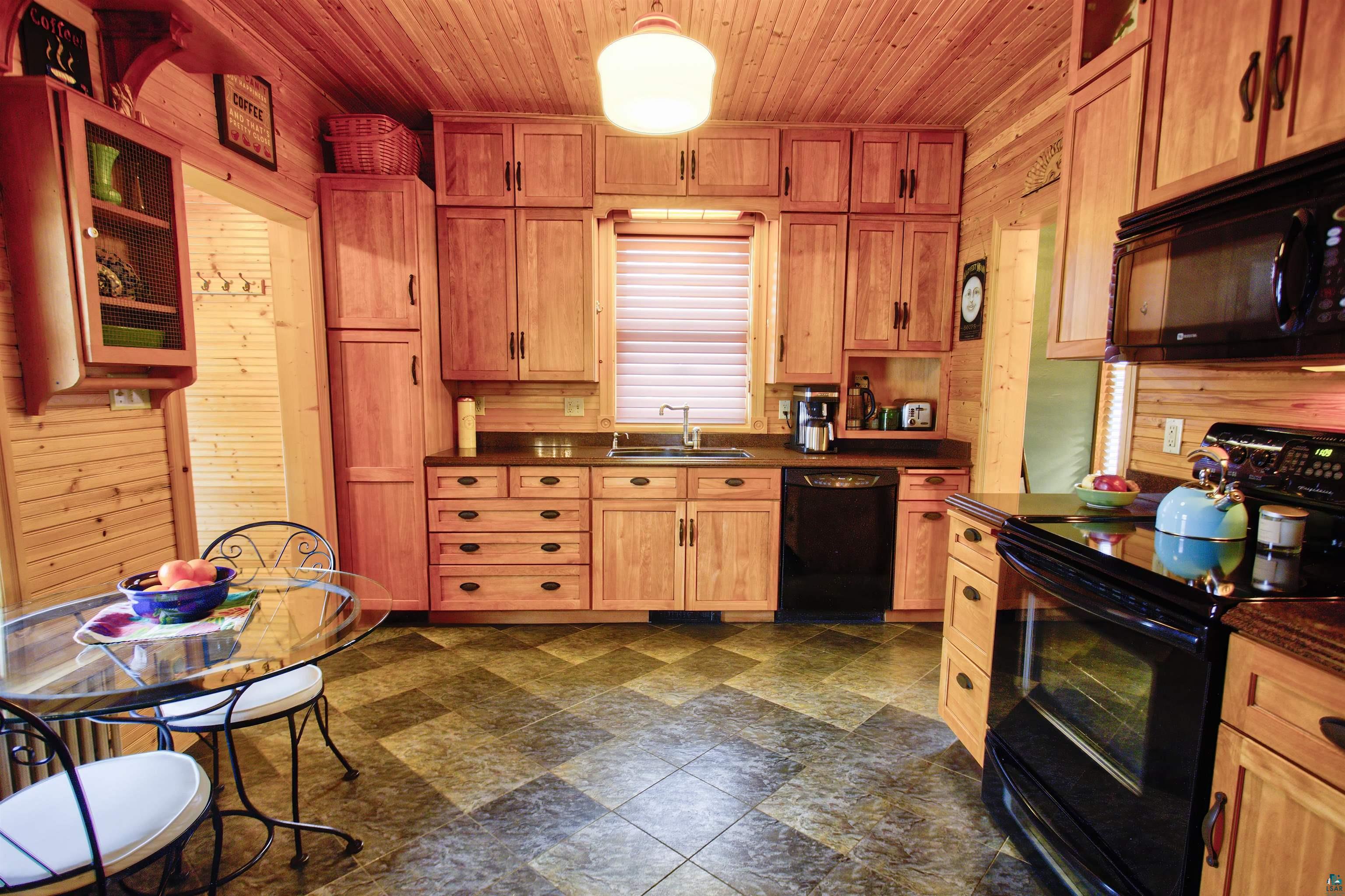 24 East Conan Street Ely, MN 55731 - Photo 10 of 27 Kitchen featuring abundant wood-finish cabinetry, black appliance suite, solid surface countertops, and patterned floor tiling