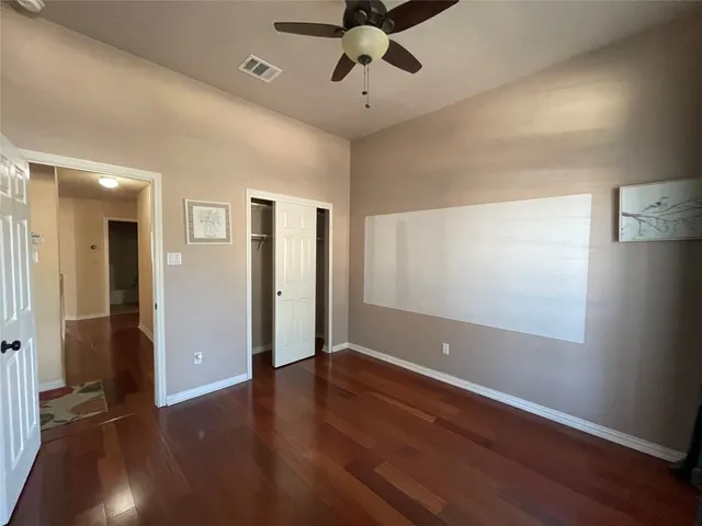 a view of an empty room with wooden floor and a ceiling fan