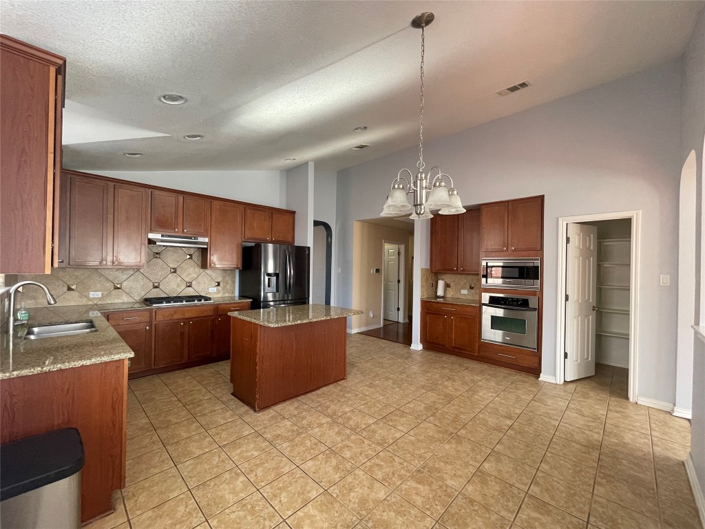 15529 Staked Plains Loop Austin, TX 78717 - Photo 5 of 32 Kitchen featuring arched walkways, tasteful backsplash, decorative light fixtures, light stone counters, and vaulted ceiling