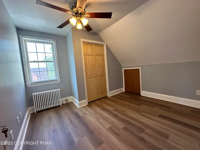 an empty room with wooden floor chandelier fan and windows
