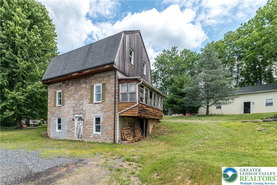 1815 Leithsville Road Hellertown, PA 18055 - Photo 35 of 38 A classic stone and wood facade with an enclosed porch, nestled among lush trees on a sprawling green lot.