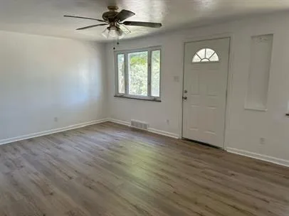 an empty room with wooden floor chandelier fan and windows