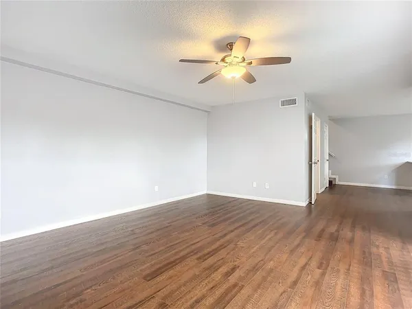 a view of an empty room with wooden floor and a chandelier fan