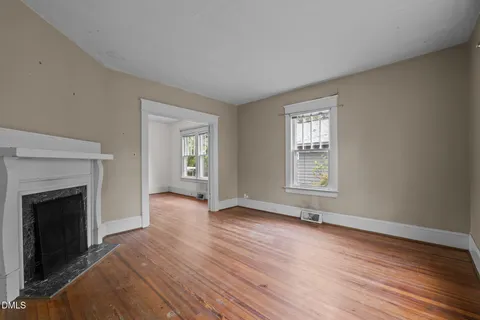 an empty room with wooden floor fireplace and windows