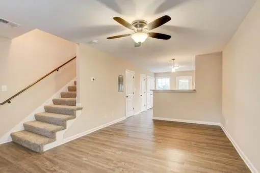 a view of an empty room with wooden floor and a ceiling fan