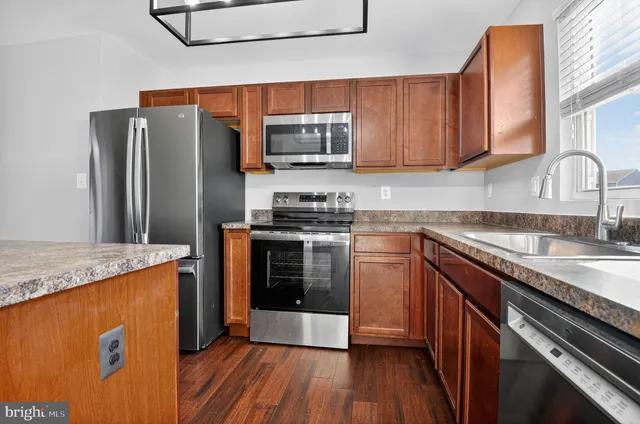 a kitchen with stainless steel appliances granite countertop a stove top oven a sink and dishwasher a refrigerator with wooden floors