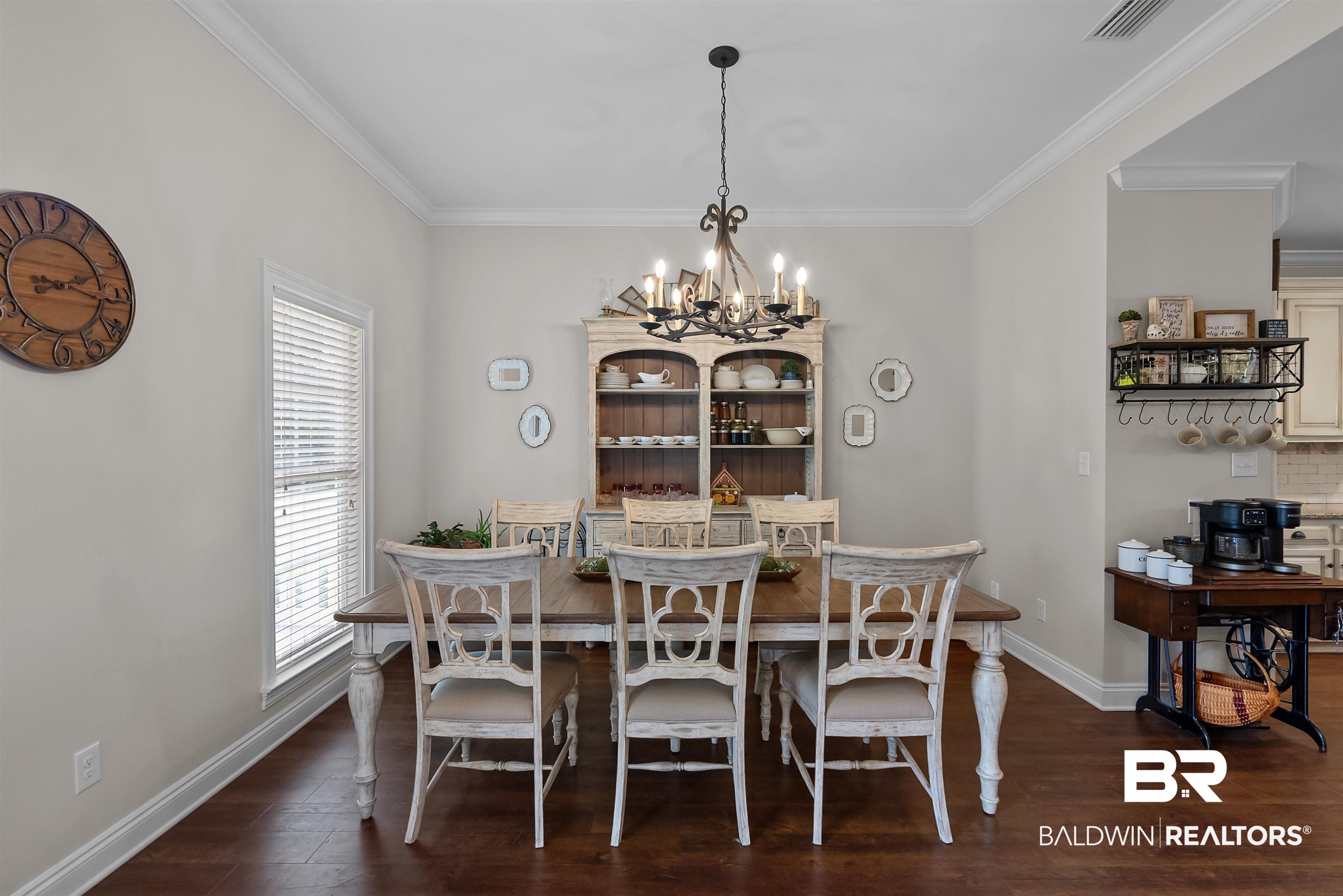 12070 Comalander Road Fairhope, AL 36532 - Photo 5 of 50 Dining space featuring wood-finish flooring, crown molding, a window with blinds, and an ornate chandelier