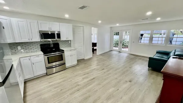 a kitchen with stainless steel appliances a stove top oven a sink dishwasher and a refrigerator with wooden floor