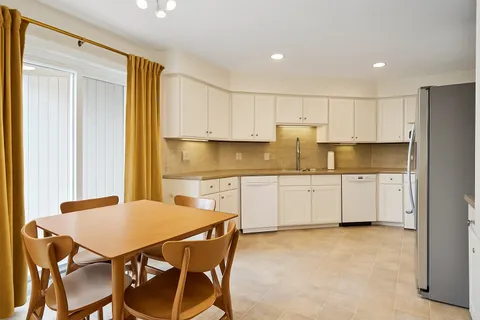 a kitchen with stainless steel appliances granite countertop a stove a refrigerator a white table and chairs with wooden floor