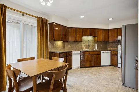 a kitchen with stainless steel appliances granite countertop a stove a refrigerator a sink a dining table and chairs