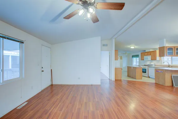 a view of an empty room and kitchen with wooden floor