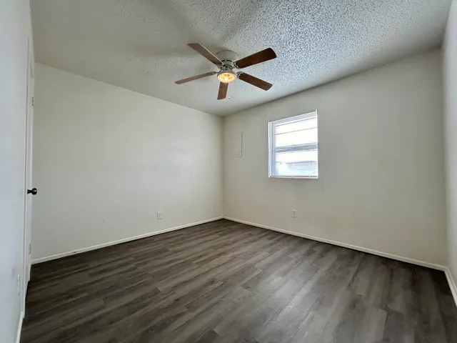 an empty room with wooden floor ceiling fan and windows