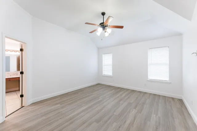 an empty room with wooden floor fan and windows