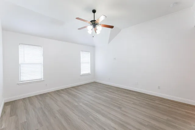 an empty room with wooden floor fan and windows