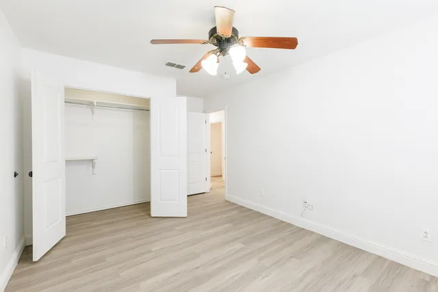 an empty room with wooden floor ceiling fan and window