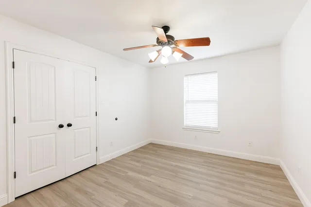 an empty room with wooden floor fan and windows