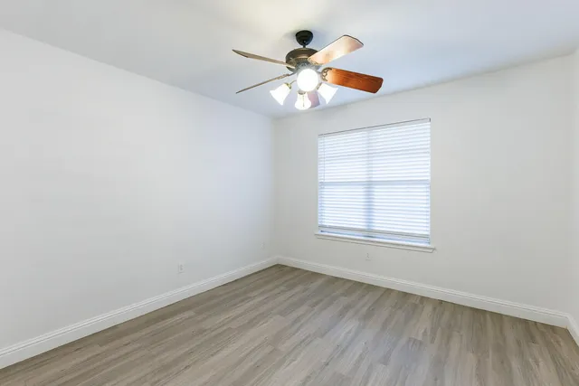 an empty room with wooden floor fan and windows