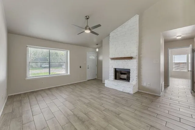 an empty room with windows a fireplace a ceiling fan and wooden floor