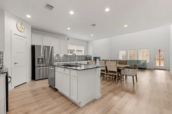 a kitchen with stainless steel appliances a refrigerator a stove a sink dishwasher and a dining table with wooden floor