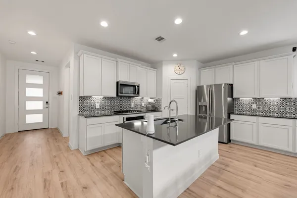 a kitchen with stainless steel appliances granite countertop a refrigerator a stove top oven a sink and dishwasher with wooden floor