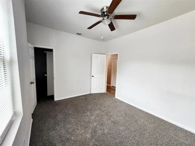an empty room with chandelier fan and windows