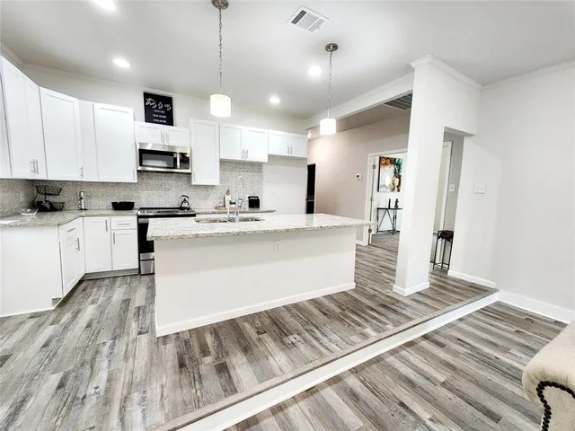 a large white kitchen with kitchen island a stove a sink dishwasher and white cabinets with wooden floor