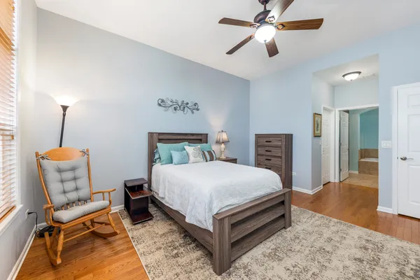 a bedroom with a bed a chair and potted plant on the dresser