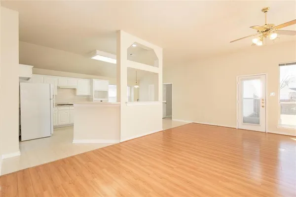 a view of an empty room with wooden floor and a kitchen