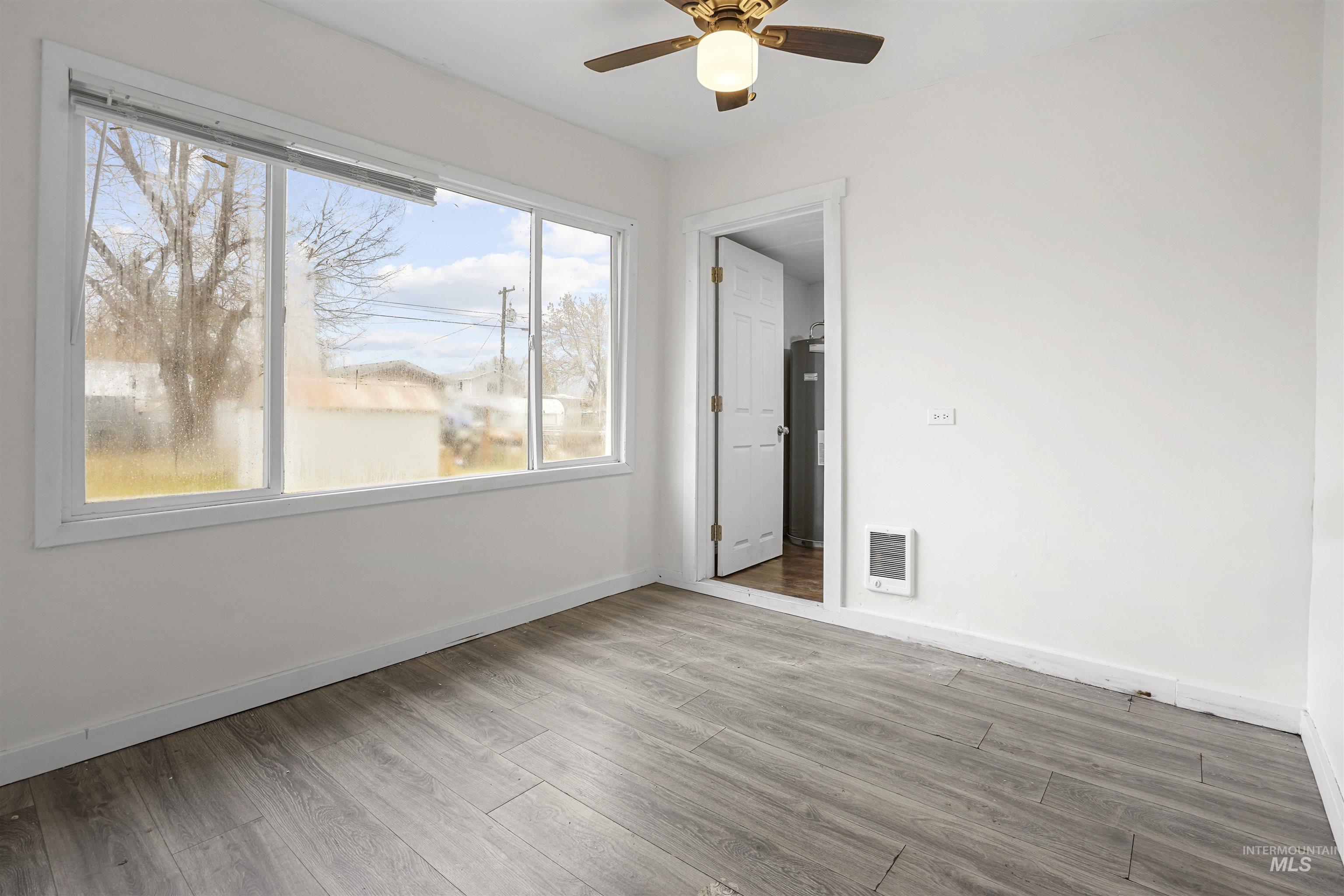 324 Linden Street Rupert, ID 83350 - Photo 6 of 13 Empty room featuring wood finished floors, ceiling fan, heating unit, and water heater