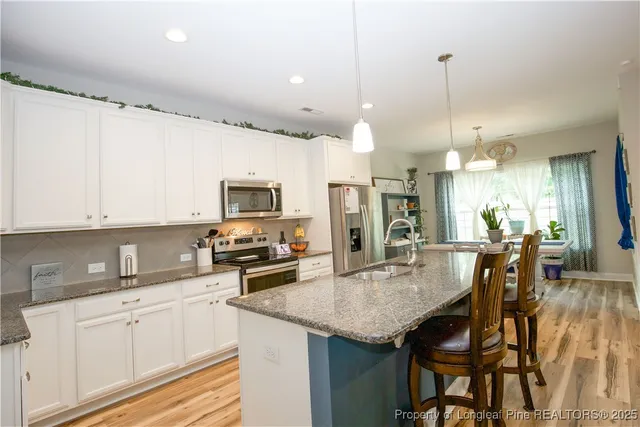 a kitchen with stainless steel appliances kitchen island granite countertop a table chairs and a refrigerator