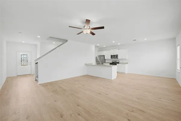 a view of empty room with wooden floor and kitchen view