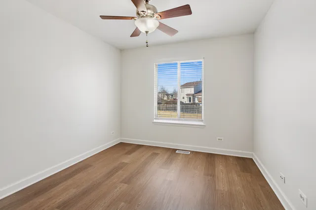 an empty room with wooden floor chandelier fan and windows