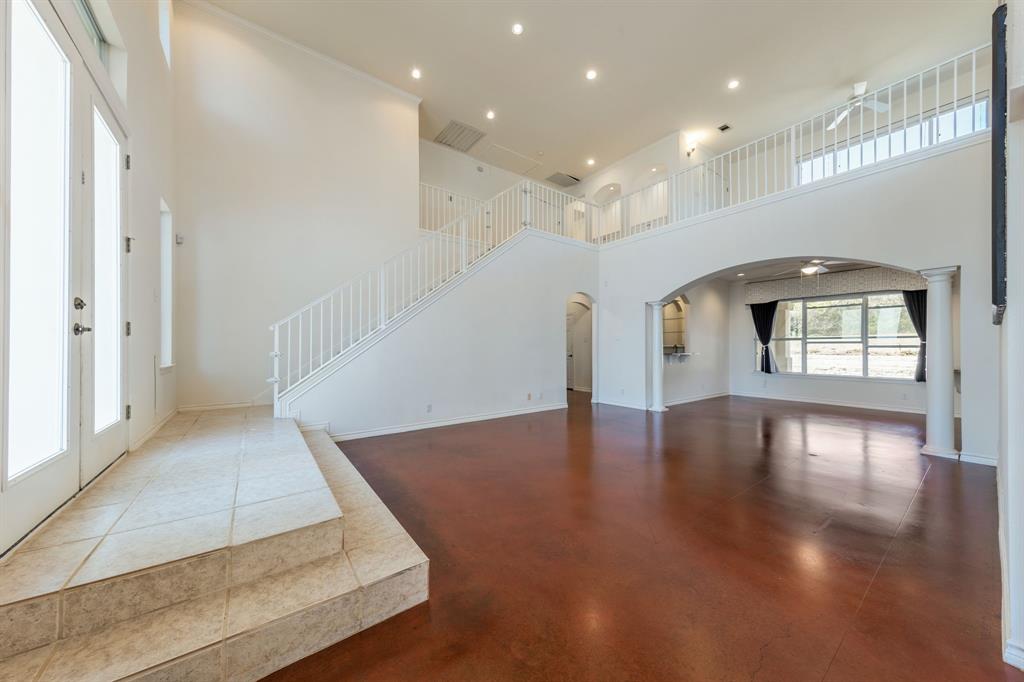 1704 Randolph Ridge Trail Austin, TX 78746 - Photo 7 of 23 Unfurnished living room featuring arched walkways, a towering ceiling, recessed lighting, concrete flooring, and stairway