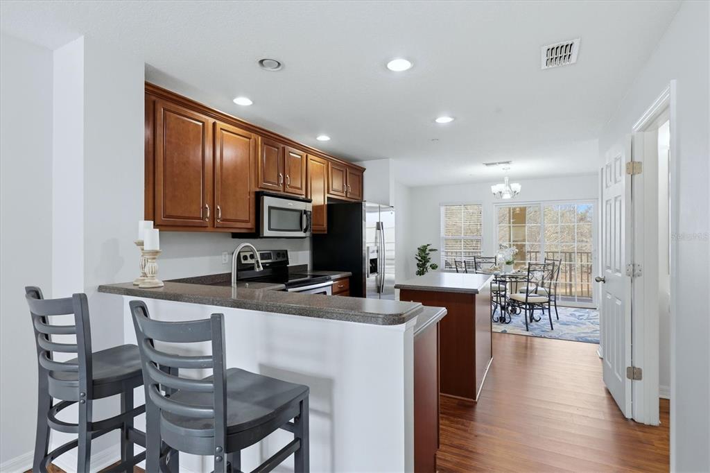 9038 White Sage Loop Lakewood Ranch, FL 34202 - Photo 14 of 52 a kitchen with stainless steel appliances granite countertop a stove top oven a sink dishwasher a dining table and chairs with wooden floor