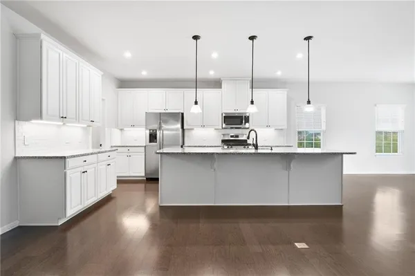 a kitchen with stainless steel appliances granite countertop a sink a stove a oven a kitchen island with white cabinets and wooden floor