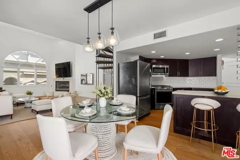 a kitchen with stainless steel appliances kitchen island granite countertop a dining table chairs and a refrigerator