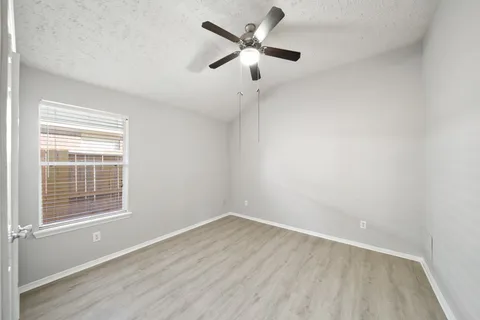 an empty room with wooden floor ceiling fan and windows