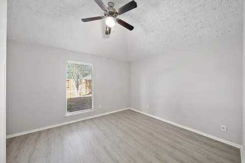an empty room with wooden floor fan and windows